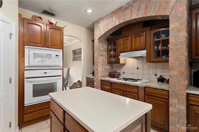 kitchen with tasteful backsplash, light tile patterned floors, a kitchen island, and white appliances