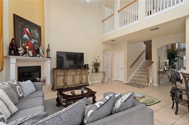 living room featuring a tile fireplace, a towering ceiling, and light tile patterned floors