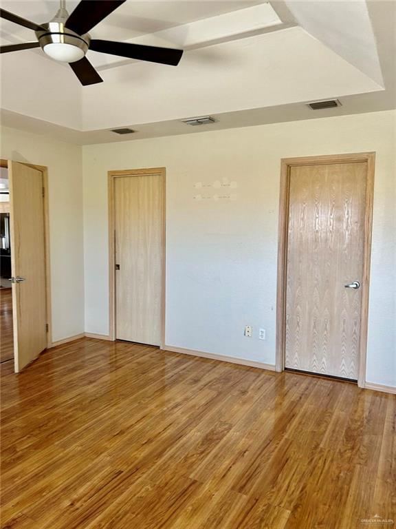 unfurnished bedroom with a tray ceiling, visible vents, and wood finished floors