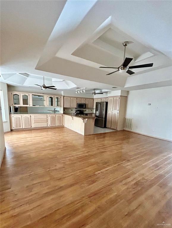 unfurnished living room with visible vents, a ceiling fan, a tray ceiling, light wood-type flooring, and a sink