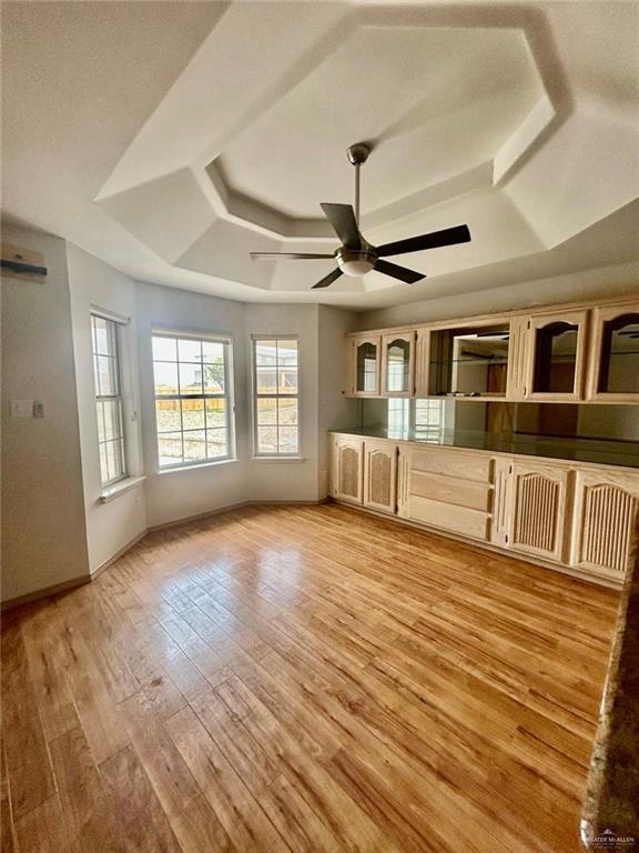 unfurnished living room with light wood finished floors, baseboards, a tray ceiling, and a ceiling fan