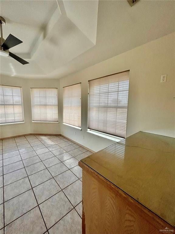 empty room with a ceiling fan, a tray ceiling, baseboards, and light tile patterned floors