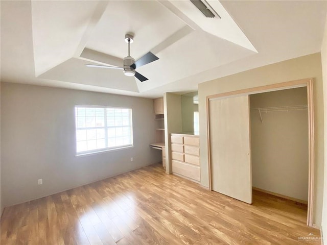 unfurnished bedroom with a closet, a raised ceiling, ceiling fan, and light wood-style flooring