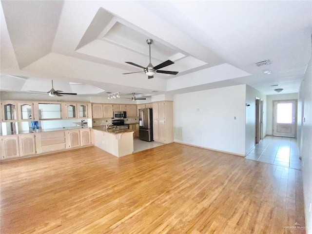 kitchen with stainless steel appliances, a raised ceiling, open floor plan, and light brown cabinetry