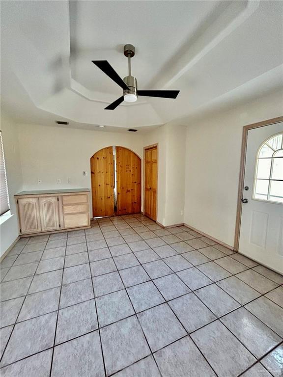 interior space with arched walkways, ceiling fan, light tile patterned floors, baseboards, and a tray ceiling