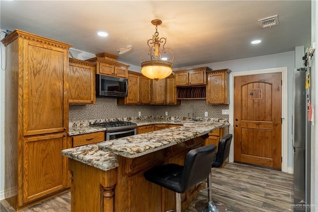 kitchen featuring a kitchen bar, light stone counters, decorative light fixtures, appliances with stainless steel finishes, and a kitchen island