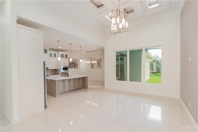 interior space with white cabinetry, stainless steel appliances, hanging light fixtures, crown molding, and a center island with sink