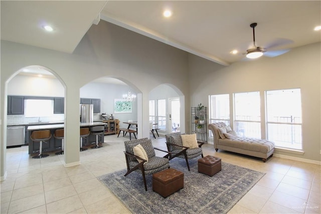 tiled living room with sink, a high ceiling, and ceiling fan with notable chandelier