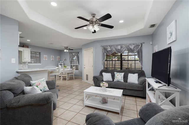 living room with light tile patterned floors, a raised ceiling, and ceiling fan