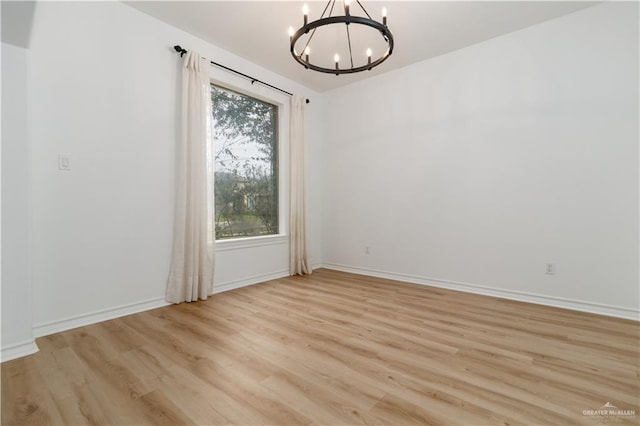 empty room with baseboards, light wood-style floors, and a notable chandelier