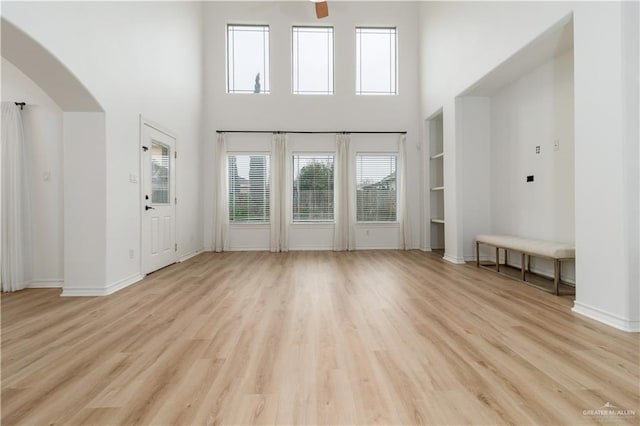 unfurnished living room with arched walkways, a high ceiling, light wood-style flooring, and baseboards