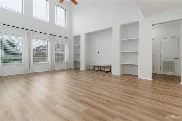 unfurnished living room featuring built in shelves, visible vents, light wood-style floors, a ceiling fan, and baseboards