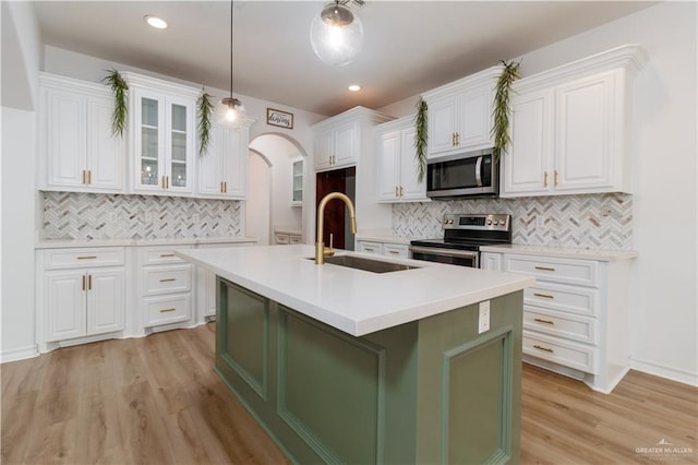 kitchen featuring white cabinets, glass insert cabinets, appliances with stainless steel finishes, light countertops, and a sink