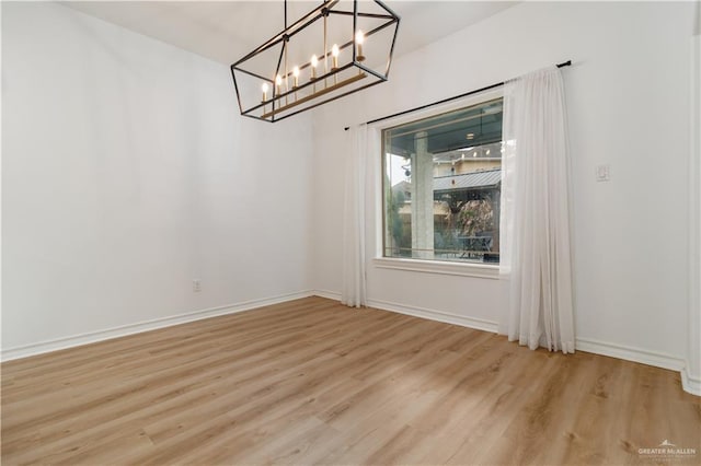 unfurnished dining area with a notable chandelier, light wood-style flooring, and baseboards