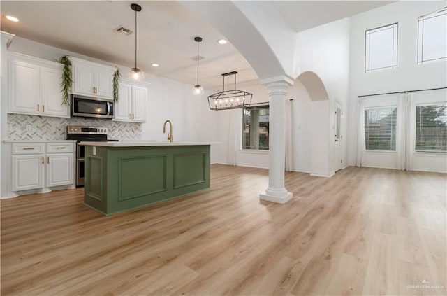 kitchen with arched walkways, decorative light fixtures, decorative columns, appliances with stainless steel finishes, and white cabinetry