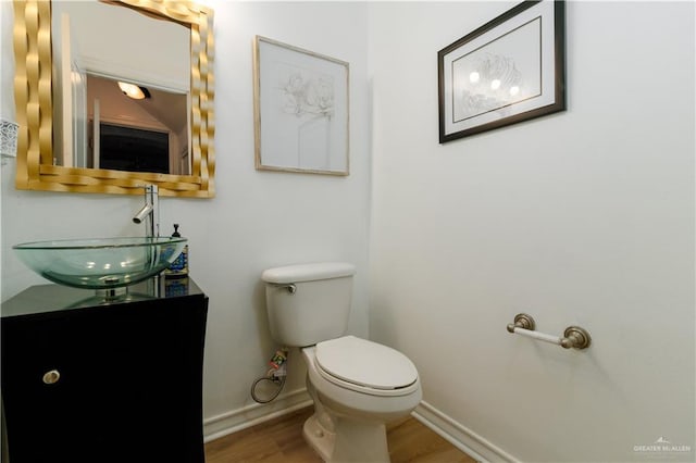 half bath with toilet, baseboards, wood finished floors, and vanity