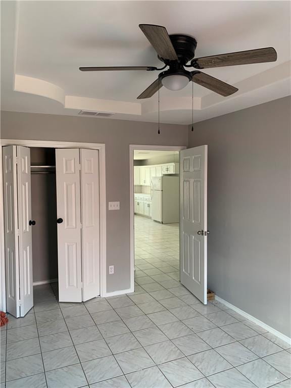 unfurnished bedroom with a raised ceiling, ceiling fan, a closet, and white refrigerator