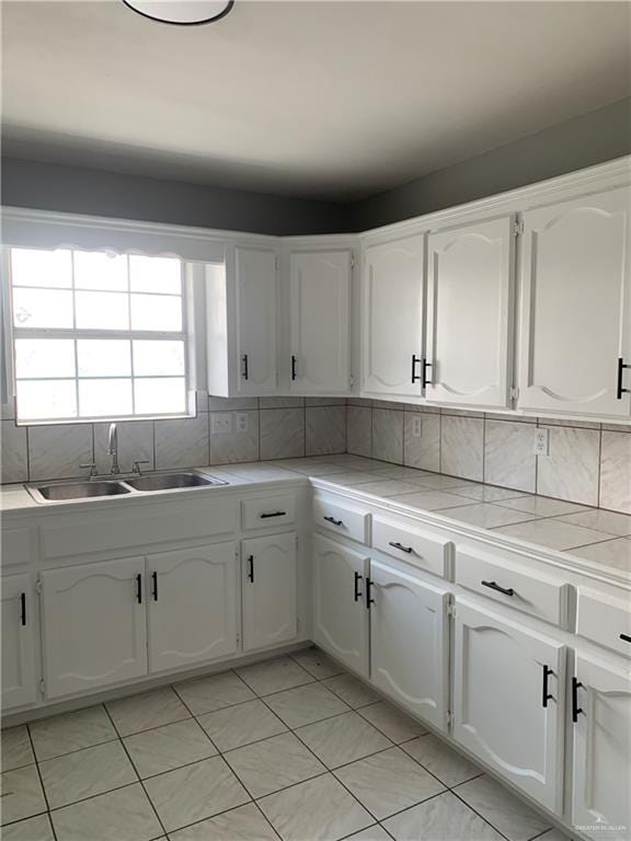 kitchen featuring tasteful backsplash, sink, tile countertops, white cabinets, and light tile patterned flooring