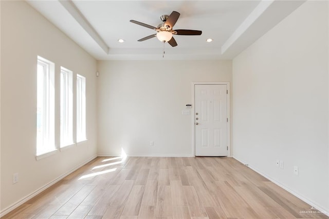 empty room with light wood finished floors, baseboards, a raised ceiling, a ceiling fan, and recessed lighting