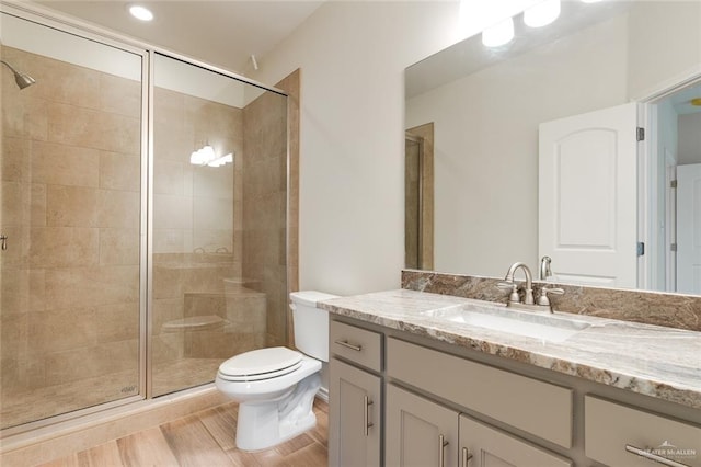 bathroom featuring wood finished floors, a stall shower, vanity, and toilet