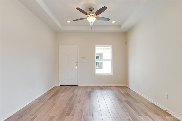 interior space featuring light wood-style flooring, baseboards, a raised ceiling, and recessed lighting