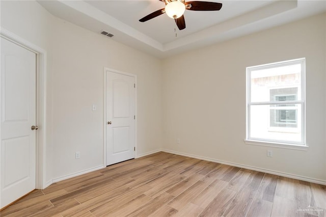 spare room with a ceiling fan, visible vents, baseboards, light wood finished floors, and a raised ceiling