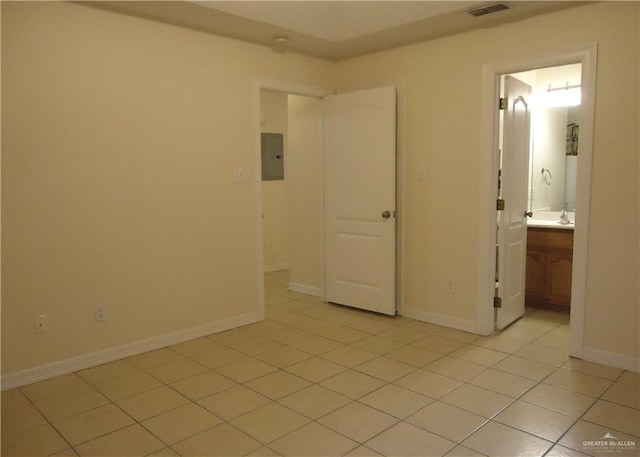 unfurnished bedroom featuring electric panel, ensuite bathroom, and light tile patterned flooring