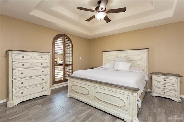 bedroom featuring ceiling fan, a raised ceiling, and wood-type flooring