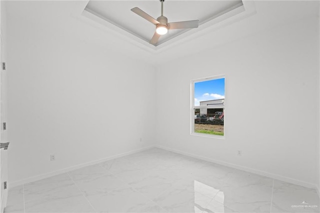 spare room with ceiling fan, marble finish floor, a raised ceiling, and baseboards