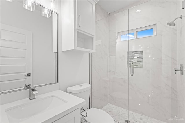 bathroom featuring toilet, a marble finish shower, and vanity