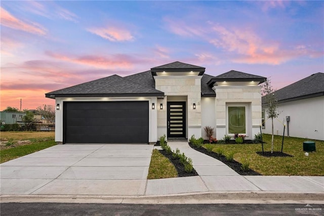 prairie-style house featuring a garage, a shingled roof, driveway, a lawn, and stucco siding