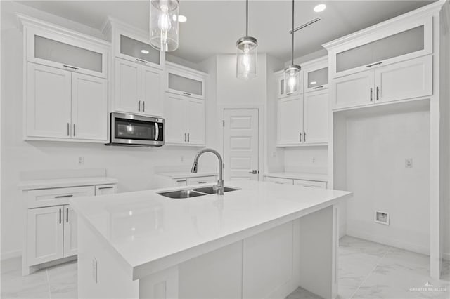 kitchen featuring marble finish floor, light countertops, stainless steel microwave, glass insert cabinets, and an island with sink