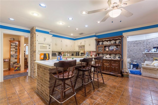 kitchen with ornamental molding, brick wall, a breakfast bar, white appliances, and ceiling fan