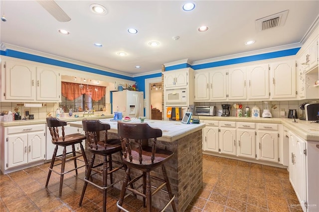 kitchen with decorative backsplash, white cabinetry, white appliances, and a breakfast bar