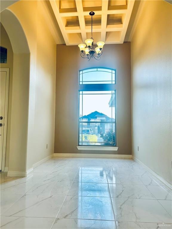 empty room featuring an inviting chandelier, coffered ceiling, beam ceiling, and a high ceiling