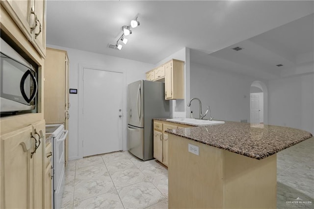 kitchen featuring kitchen peninsula, appliances with stainless steel finishes, dark stone counters, sink, and light brown cabinets