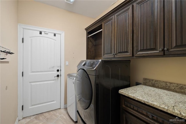 clothes washing area featuring separate washer and dryer, light tile patterned floors, cabinet space, and baseboards