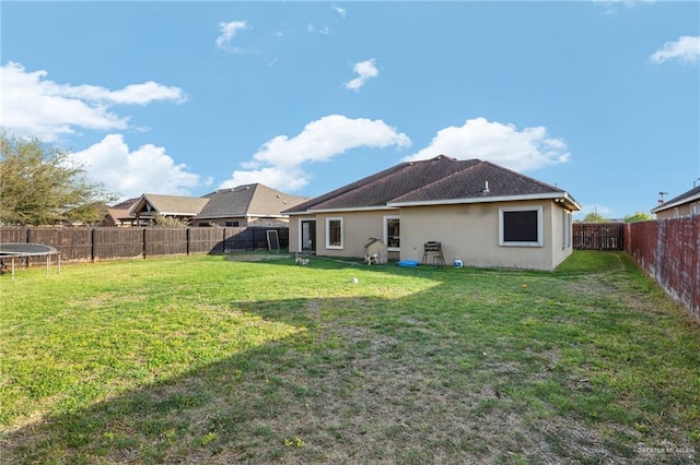 back of property with stucco siding, a trampoline, a fenced backyard, and a lawn