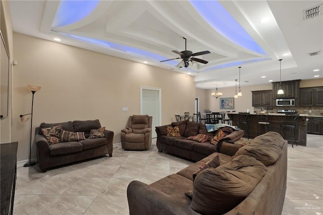 living room featuring a raised ceiling, recessed lighting, ceiling fan with notable chandelier, and visible vents