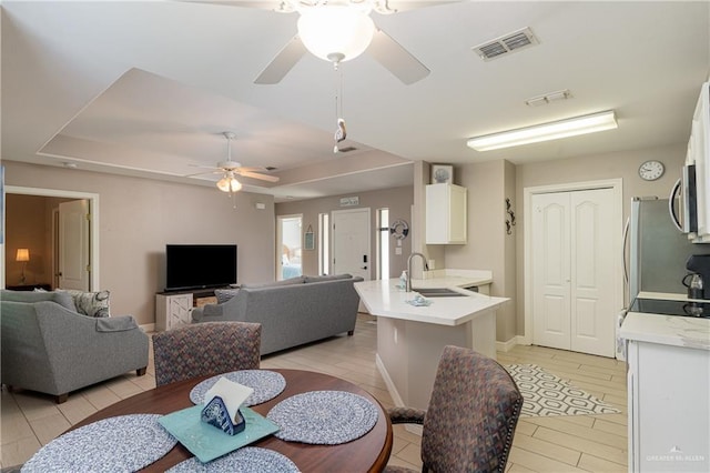 dining area featuring ceiling fan, a raised ceiling, and sink