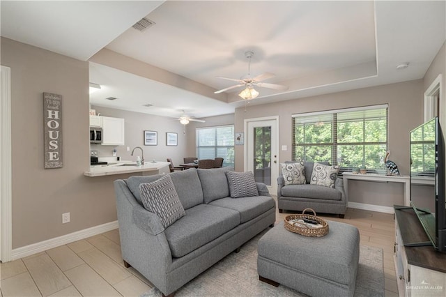 living room with a raised ceiling, ceiling fan, and light hardwood / wood-style flooring