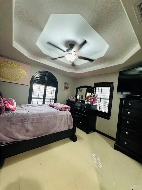 bedroom with ceiling fan, a raised ceiling, and multiple windows