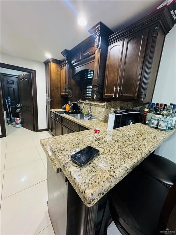 kitchen featuring light stone countertops, kitchen peninsula, sink, and dark brown cabinetry