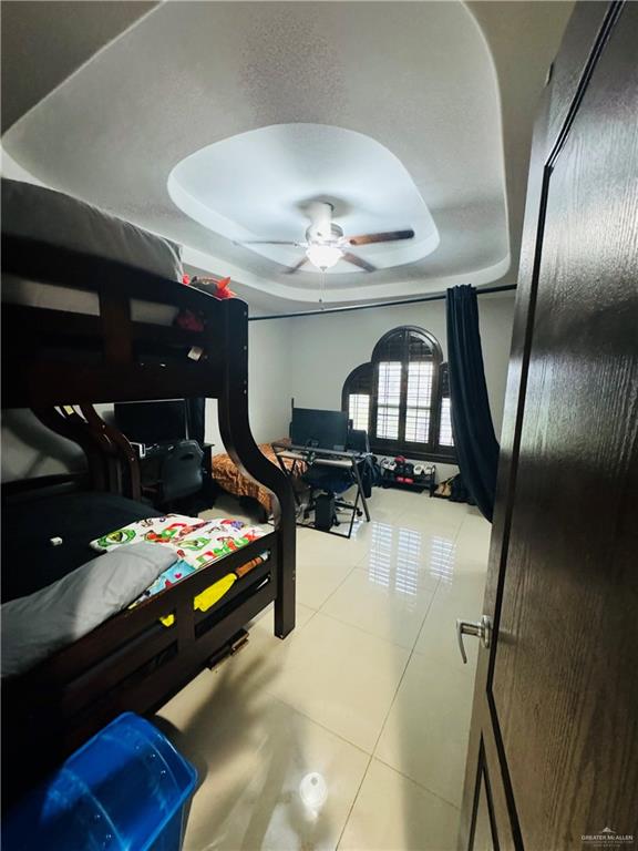 bedroom with a tray ceiling, tile patterned floors, and ceiling fan