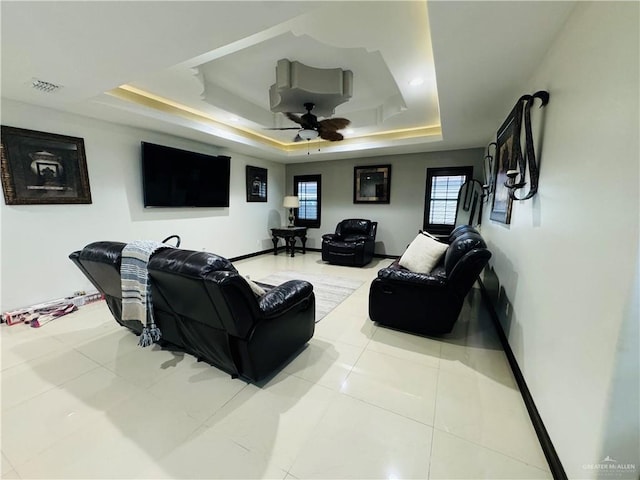 living room with light tile patterned floors, a raised ceiling, and ceiling fan