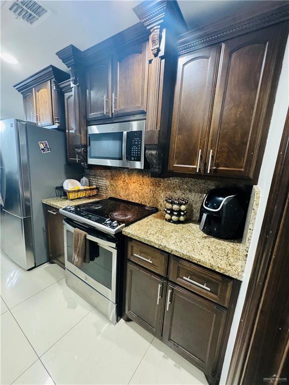 kitchen with dark brown cabinetry, stainless steel appliances, tasteful backsplash, light stone counters, and light tile patterned floors