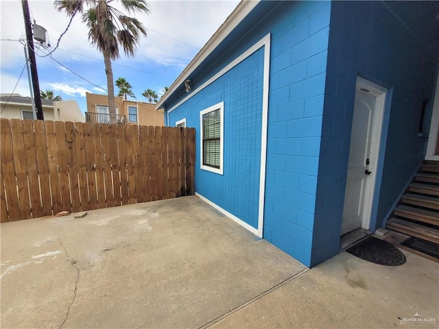 view of side of property with concrete block siding, a patio area, and fence
