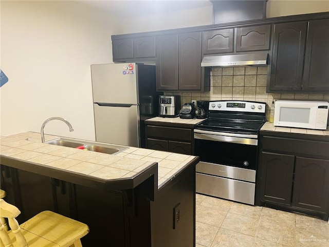 kitchen featuring sink, backsplash, tile countertops, light tile patterned flooring, and appliances with stainless steel finishes