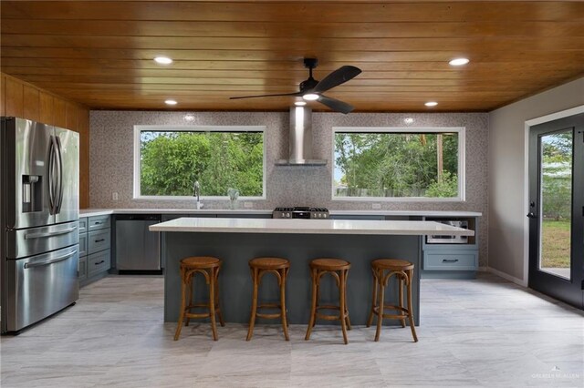 kitchen with appliances with stainless steel finishes, a center island, gray cabinetry, and wall chimney exhaust hood