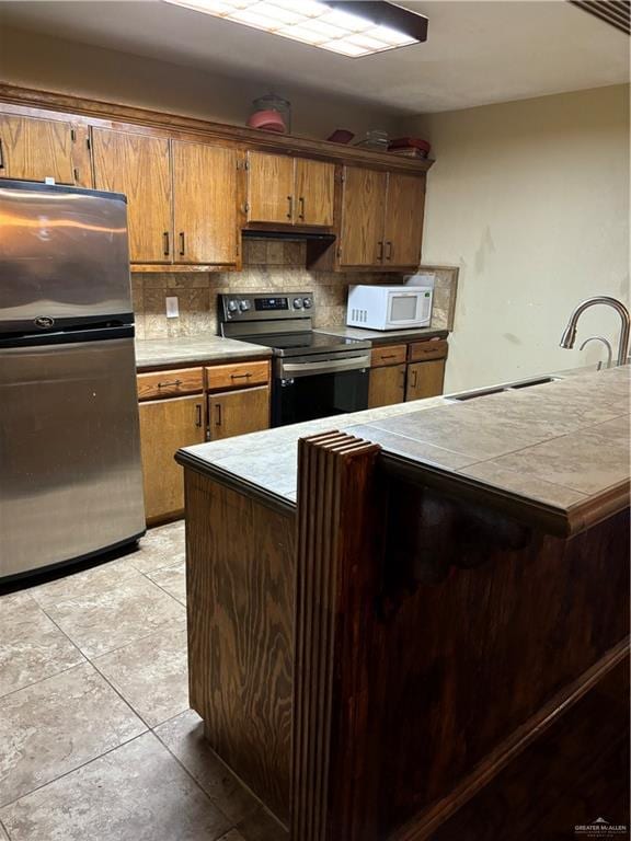 kitchen with sink, kitchen peninsula, decorative backsplash, light tile patterned floors, and appliances with stainless steel finishes